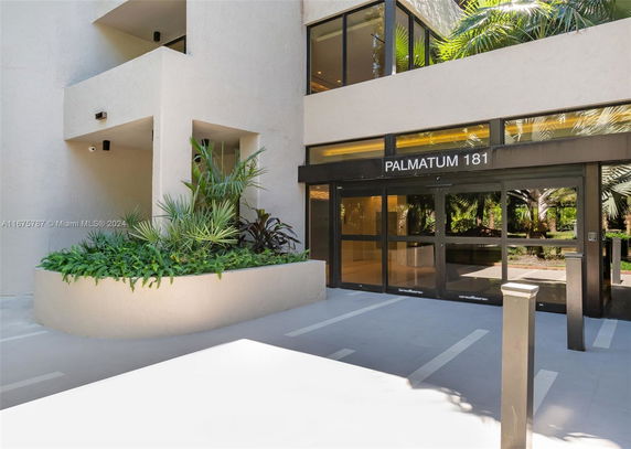 Front view of a building entrance with glass doors and surrounding greenery.