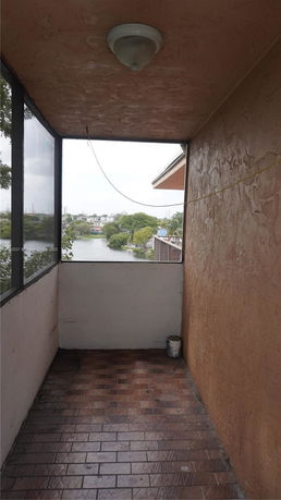 A narrow outdoor space with tiled flooring and a view overlooking a river and trees in the distance.