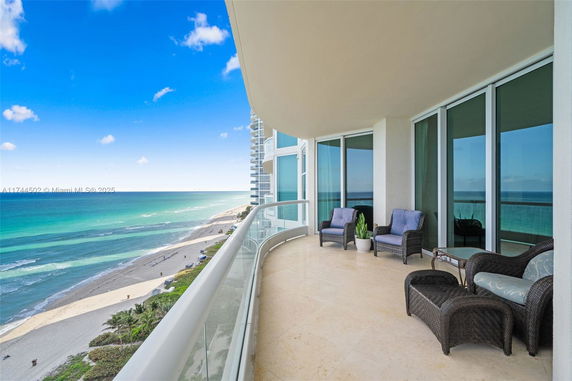 Balcony view overlooking the ocean and beach with outdoor seating.