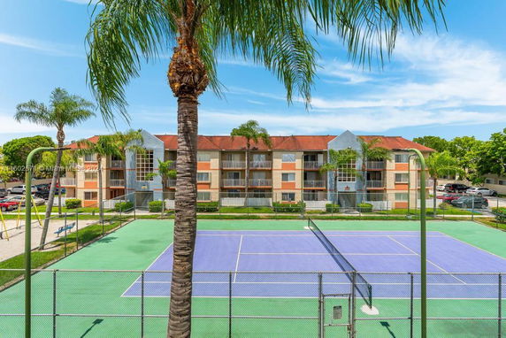 View of a multi-story residential building with a tennis court in front.