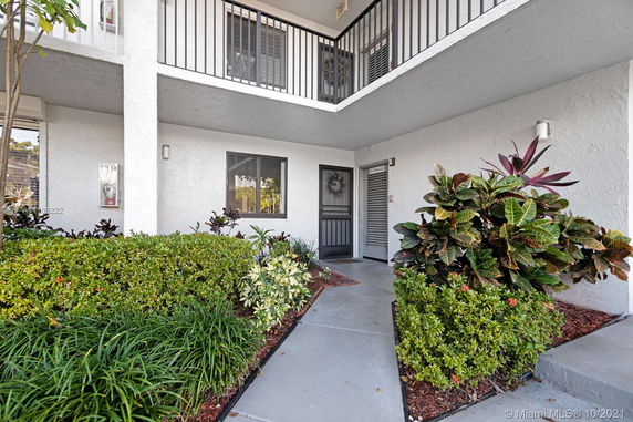 Front view of a two-story building with white walls and black railings, featuring a small entrance area with plants.