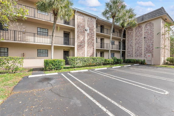 Front view of a multi-story residential building with balconies and adjacent parking spaces.