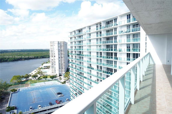View from a high balcony overlooking parking, residential buildings, and a waterfront area.