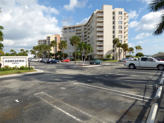 Front view of a multi-story residential building with balconies and a parking lot in the foreground.