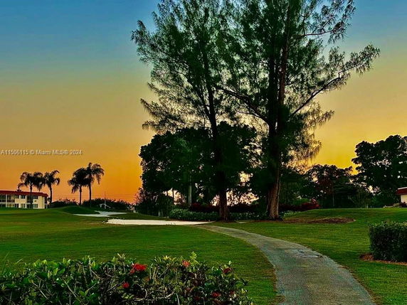 Sunset view of a landscaped area with trees and a pathway, with buildings in the background.