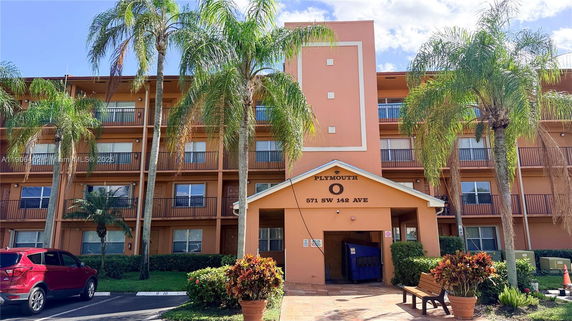Front view of a multi-story residential building with balconies and surrounding palm trees.