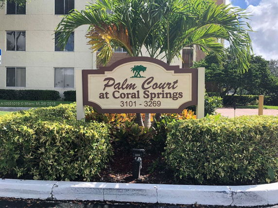 Front view of a building with a sign reading 'Palm Court at Coral Springs' and an address.