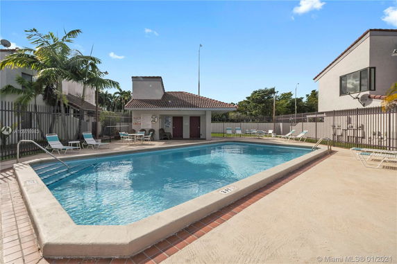 Outdoor swimming pool area with lounge chairs and small building in the background.