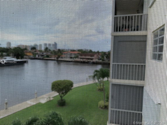 View from a window showing part of a building structure and the surrounding area with water and trees visible in the background.