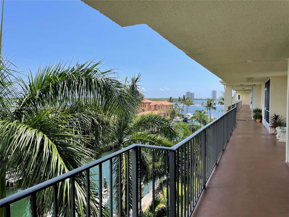 View from an apartment balcony overlooking palm trees and a body of water with buildings in the distance.