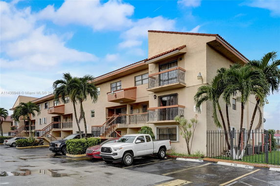 Front view of a multi-story apartment building with balconies and parked vehicles.