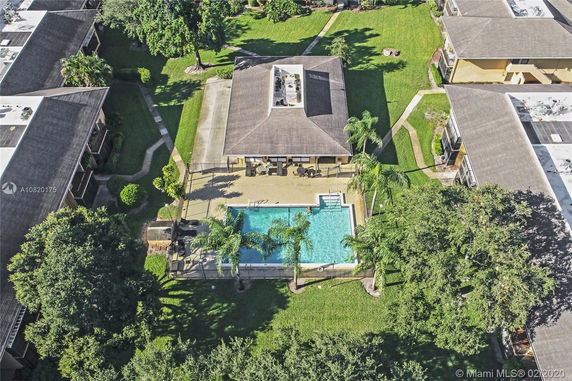 Aerial view of a small rectangular building surrounded by greenery, with a swimming pool and palm trees in front.