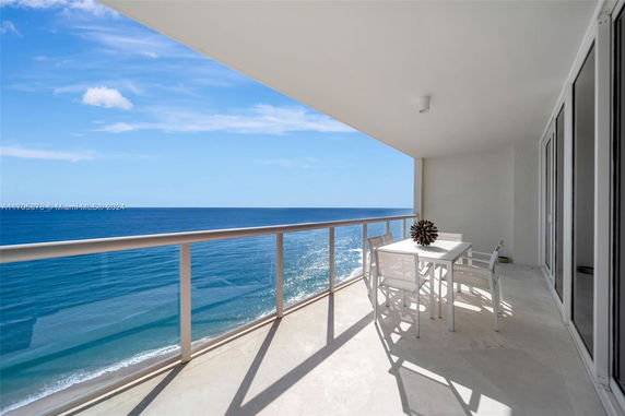 Balcony with a dining table overlooking the ocean and clear sky.