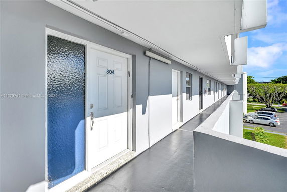 Outdoor corridor of a building with apartment doors and view of parked cars below.