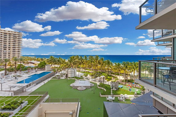 Panoramic view from a building showing a pool, greenery, and ocean in the background.