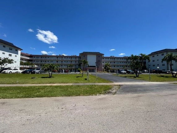 Front view of a large multi-story building with multiple windows and a parking area in front.