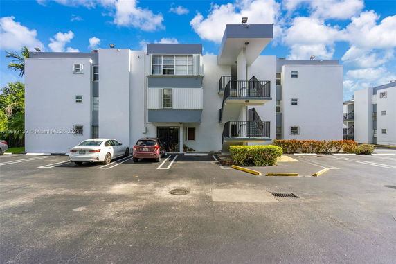 Exterior view of a multi-story building with a parking area in front.