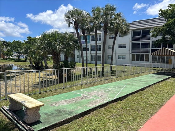 View of a multi-story residential building with a shuffleboard court and palm trees.