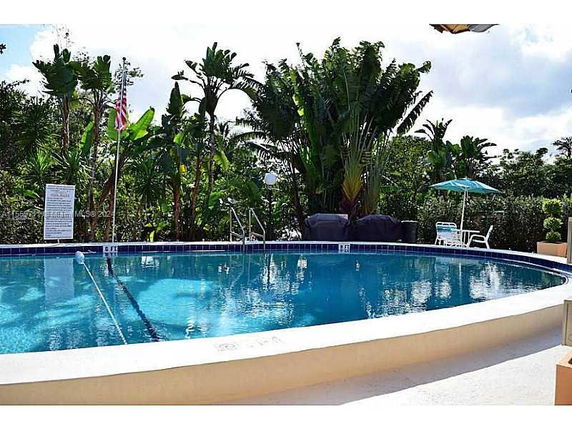 Outdoor swimming pool with surrounding tropical plants and seating area.