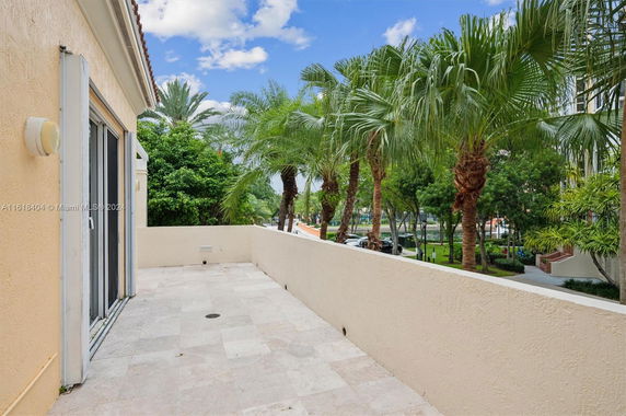 View from a terrace with tiled flooring, overlooking palm trees and adjacent buildings.