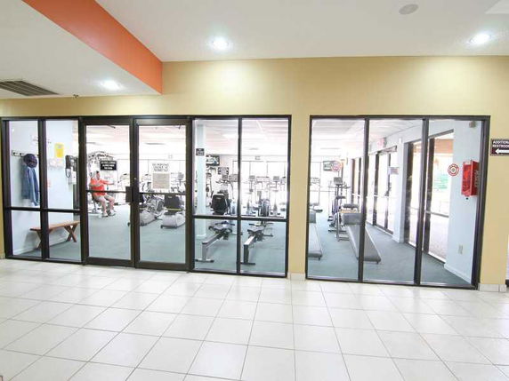 Interior view of a gym with exercise equipment visible through glass walls.