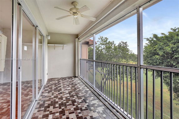 Balcony with tiled floor and ceiling fan overlooking green area and trees.