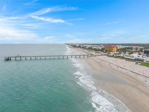 Aerial view of a coastal city with a long pier extending into the ocean and a sandy beach along the shoreline.