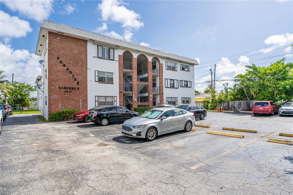Front view of a three-story residential building with a parking area in front.