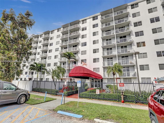 Front view of a multi-story apartment building with balconies and a red awning entrance.