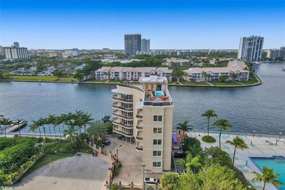 A multi-story building by a waterfront with a rooftop pool and surrounding residential buildings.