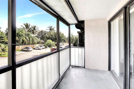 Outdoor view from a building balcony overlooking a parking area with parked cars and surrounding trees.