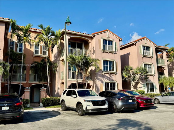 Front view of a three-story residential building with balconies and parked cars.