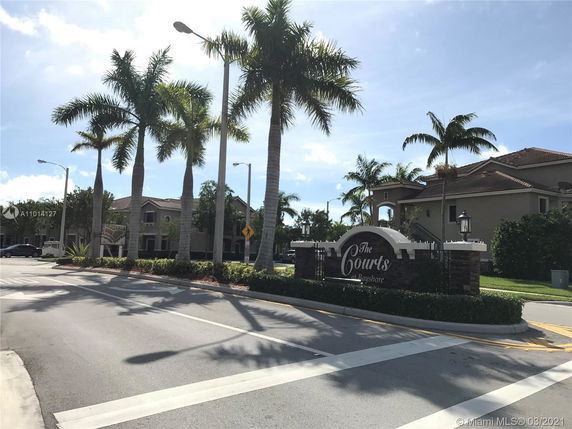 Front view of a residential complex entrance with palm trees.