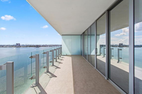Balcony with glass railing overlooking water and cityscape in the background.