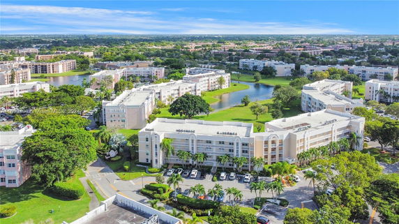 Aerial view of residential buildings surrounded by greenery and a small lake.