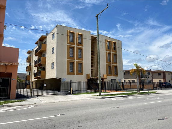 Front view of a multi-story apartment building with balconies and gated entrance.