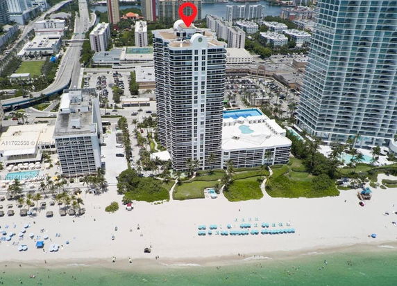 Aerial view of a beachfront high-rise building with a swimming pool on the roof and a beach in the foreground.