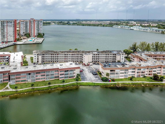 Aerial view of waterfront apartment buildings with a lake and cityscape in the background.