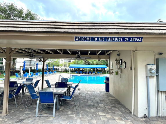 Outdoor seating area under a covered patio near a swimming pool.