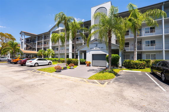 Front view of a multi-story residential building with balconies and a parking area in front.