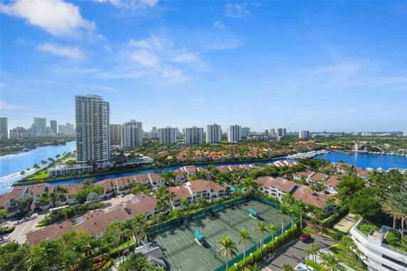 Panoramic view of a cityscape with residential buildings, a waterway, and tennis courts.