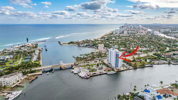 Aerial view of a coastal area with a large body of water, nearby bridge, lighthouse, and residential buildings.