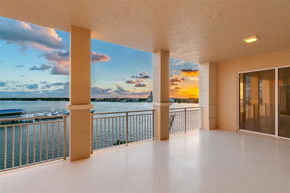 Covered balcony with railing overlooking a waterfront view and sunset.