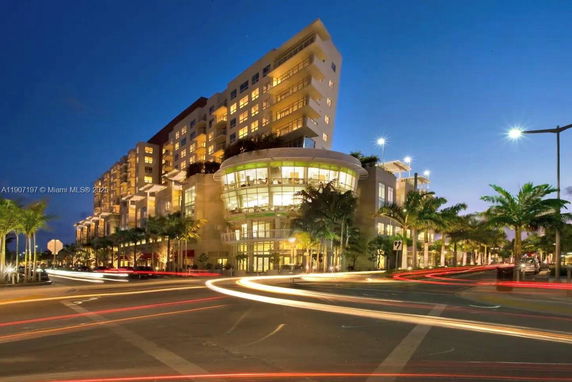 Front view of a multi-story building at night with illuminated windows and palm trees.