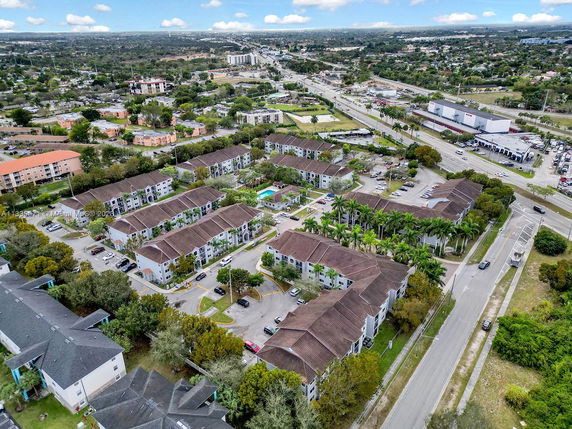 Aerial view of a residential complex with multiple apartment buildings, parking areas, and surrounding roads.