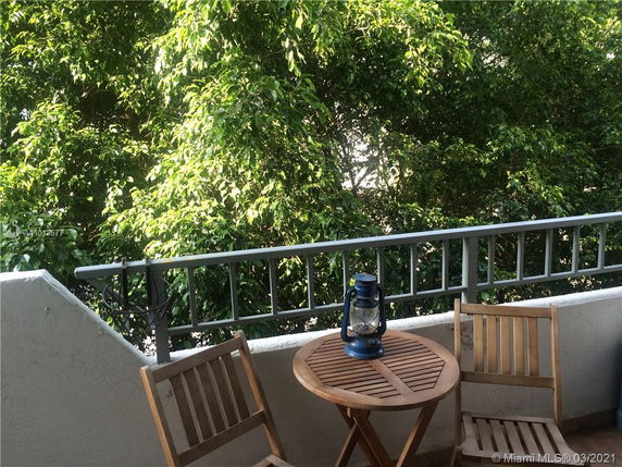 View from a balcony with a small wooden table and chairs, looking out onto green trees.