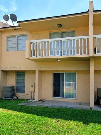 Rear view of a two-story house with a small balcony and sliding glass doors.