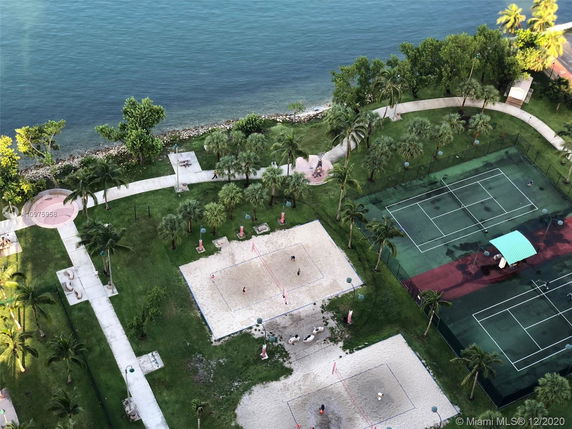 Aerial view of recreational area with tennis courts, sand volleyball courts, and walkways by the water.