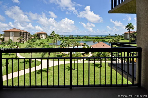 Balcony view of residential buildings with well-maintained gardens and a distant ocean backdrop.