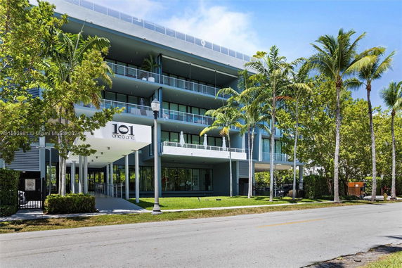 Front view of a modern multi-story building with balconies and palm trees.